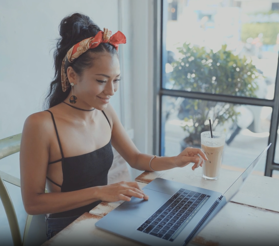 Smiling Lashify affiliate creating content from a cozy cafe with her laptop and iced latte.